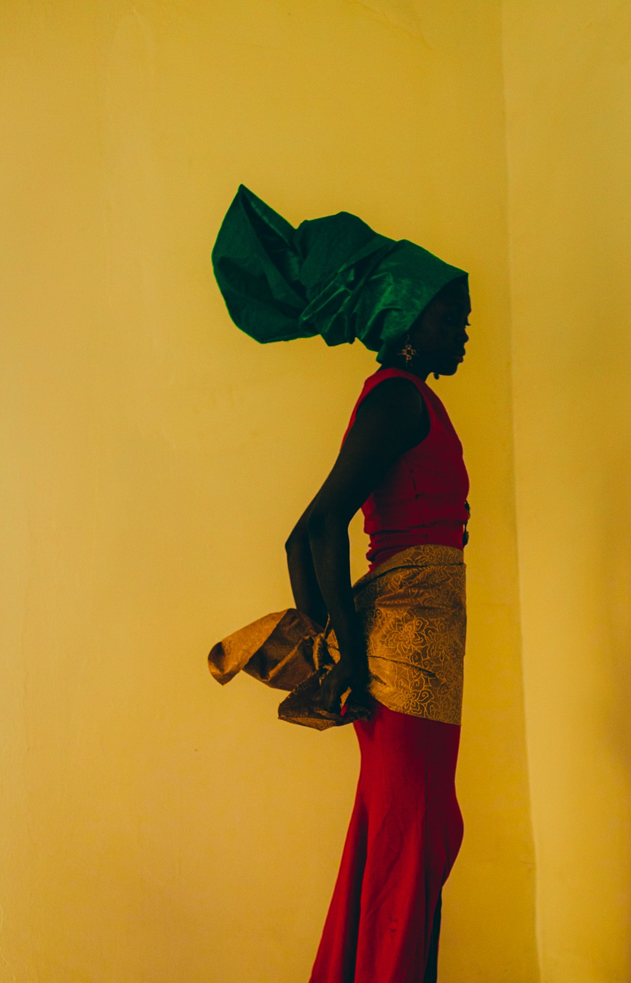Black woman in red dress and green headdress in yellow room