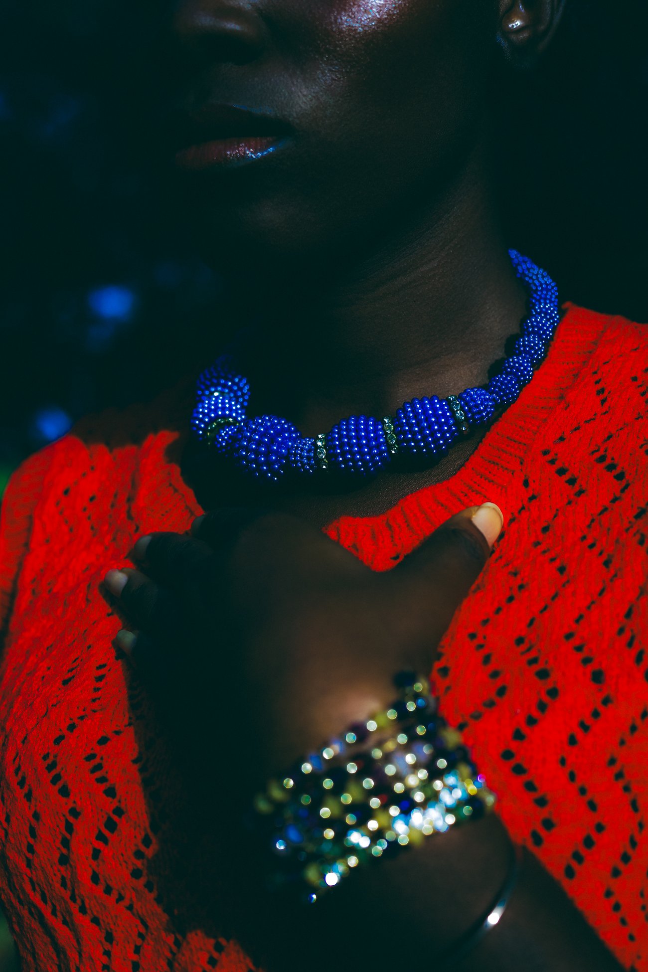 Close up of Black woman’s neck wearing a blue beaded necklace and red sweater