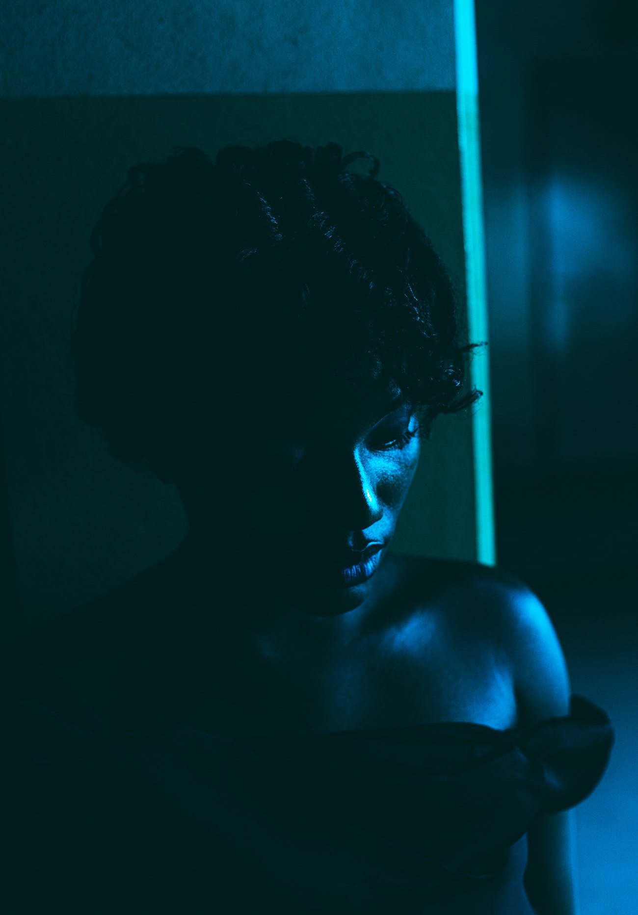 Black woman in shoulderless dress looking down in blue lit room