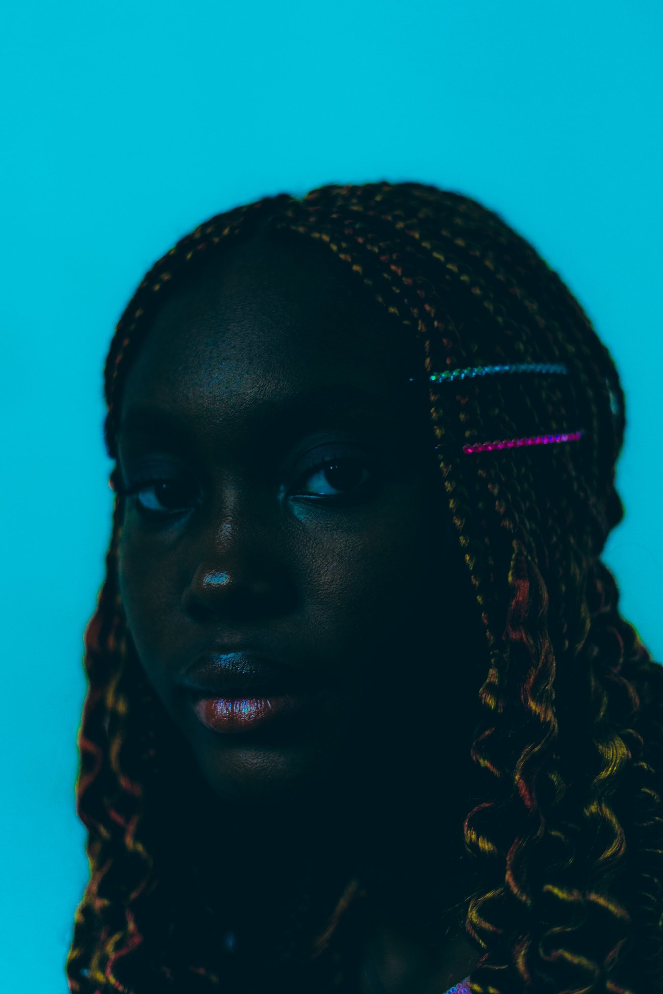 Close up portrait of Black woman with curled braids looking at camera with turquoise background