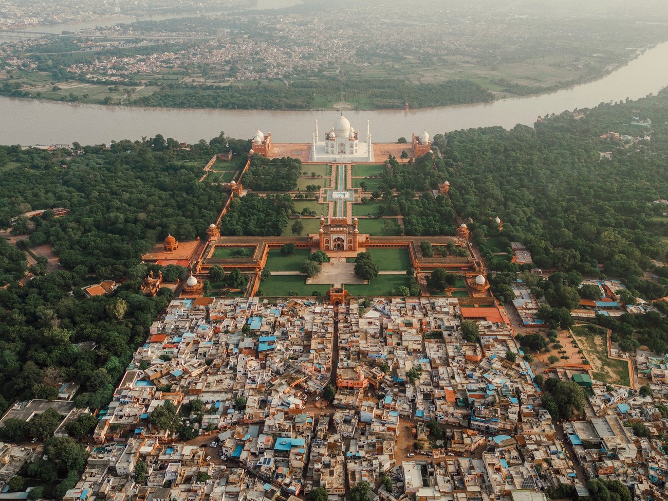 Taj Mahal in India pictured from above showing it surrounded by trees, a river and the neighboring roofs of shops and houses