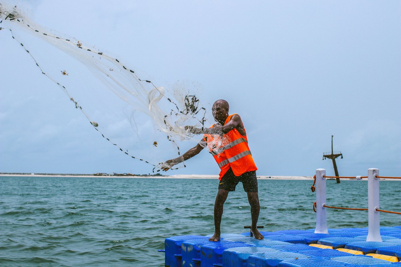 Black man in life vest throwing fishing net from blue pier