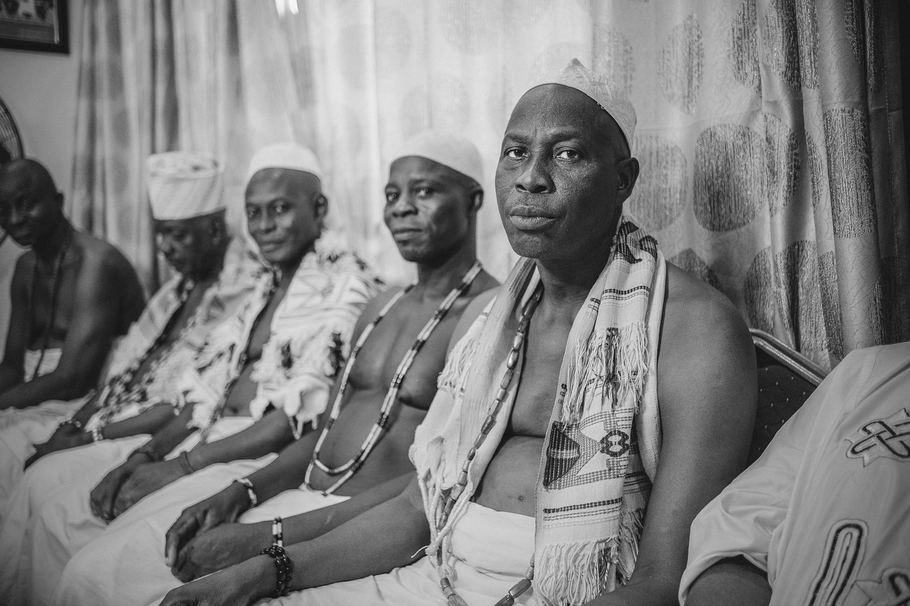 Shirtless Black men sitting together wearing scarves, beads and Kufi hats