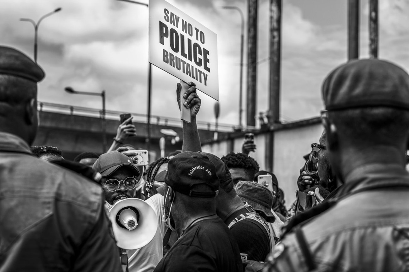 Protest with central Black man holding megaphone and “Say No To Police Brutality” sign