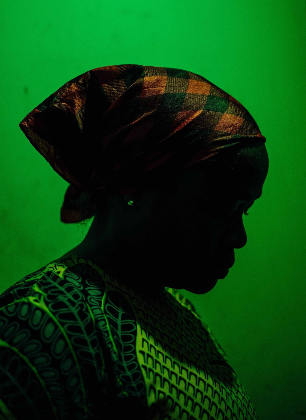Silhouette side view of Black woman looking down with her hair wrapped in scarf, in green lit room