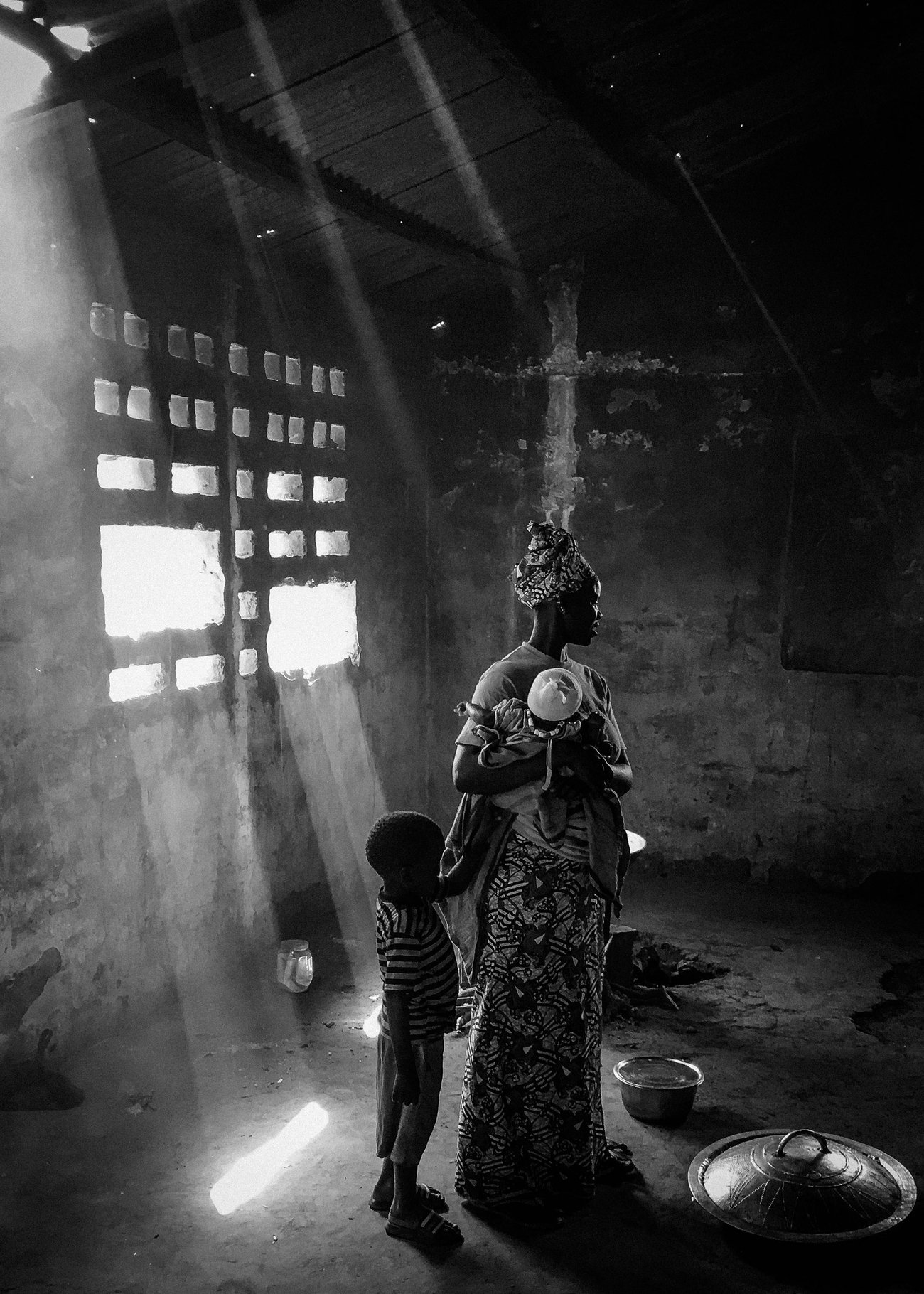 Black woman in African headdress holding new born baby to her chest with little boy at her side