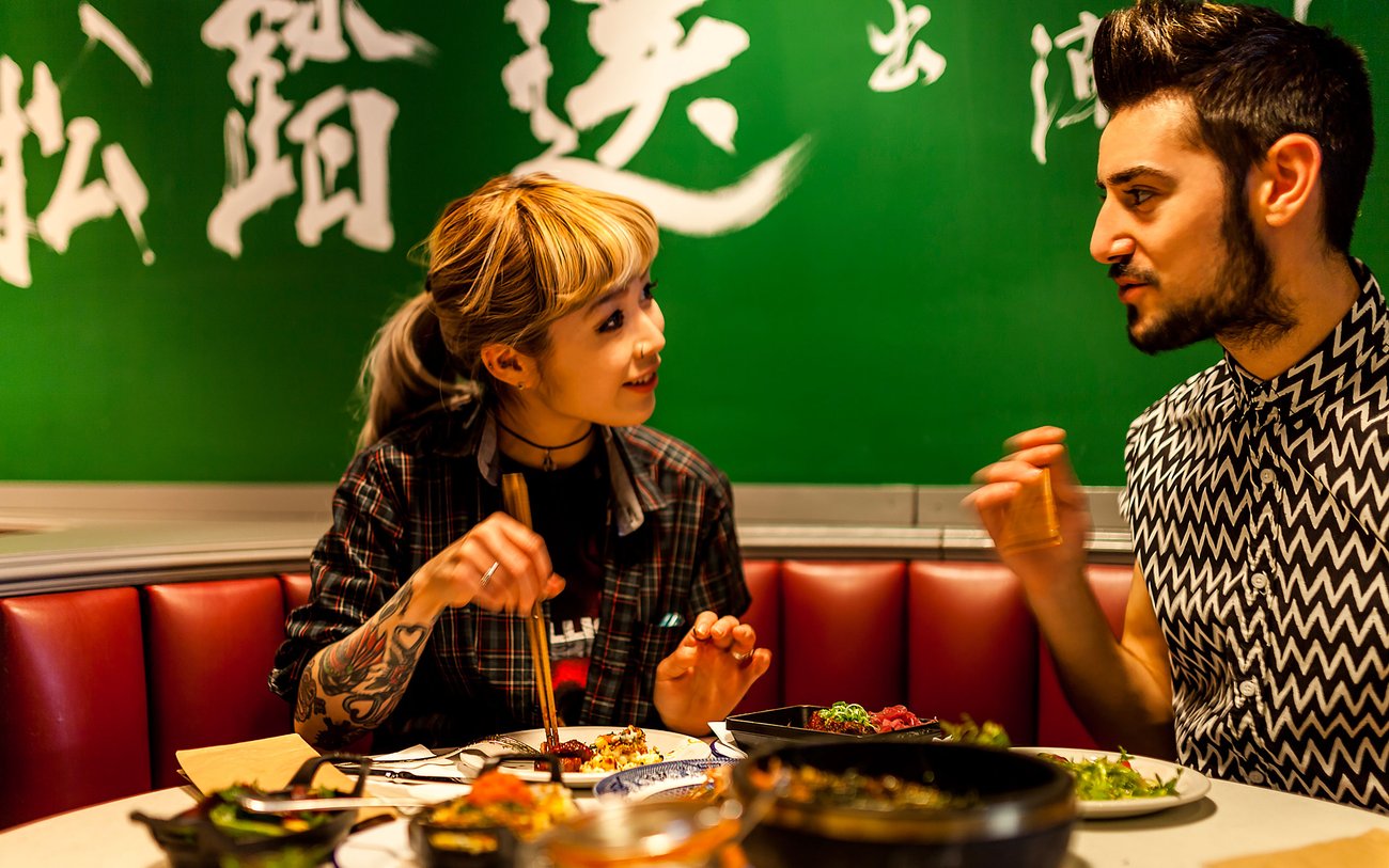 Woman and man talk over meal in Asian restaurant with green wall with Chinese characters