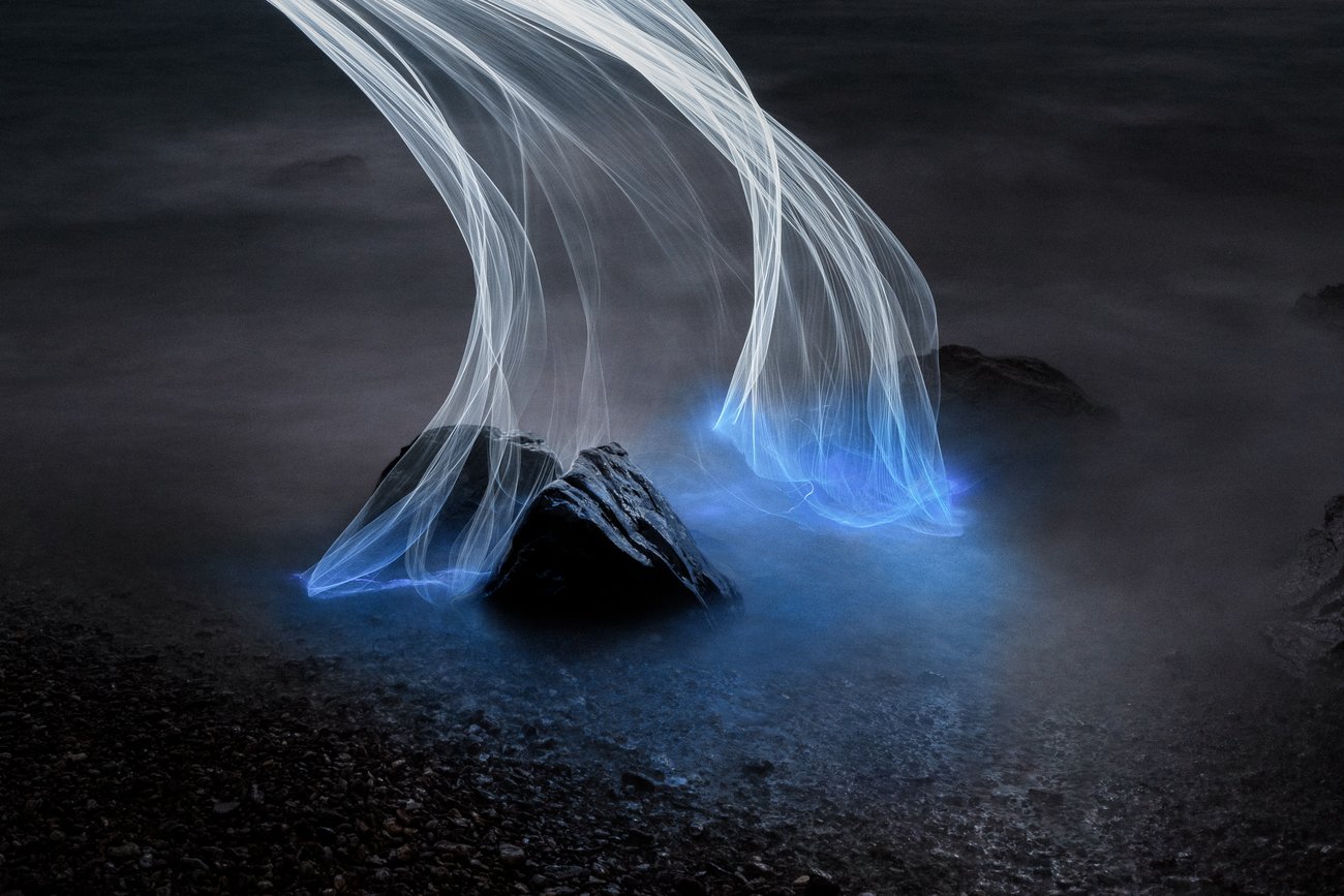 Multiple threads of thin light giving the effect of blue steam being released from two rocks at night