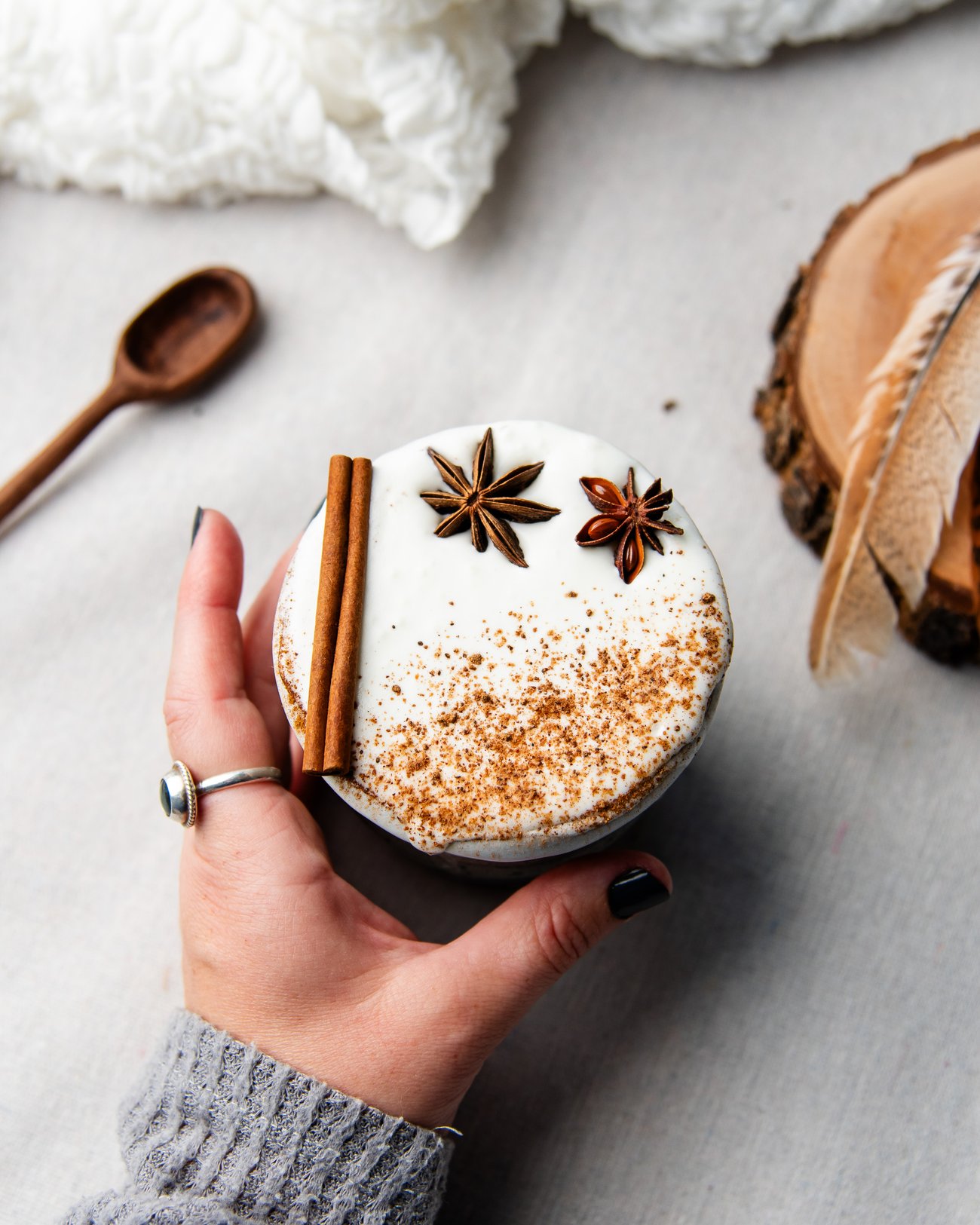 Top view of female hand reaching for frothy milk beverage topped with cinnamon stick and star anise