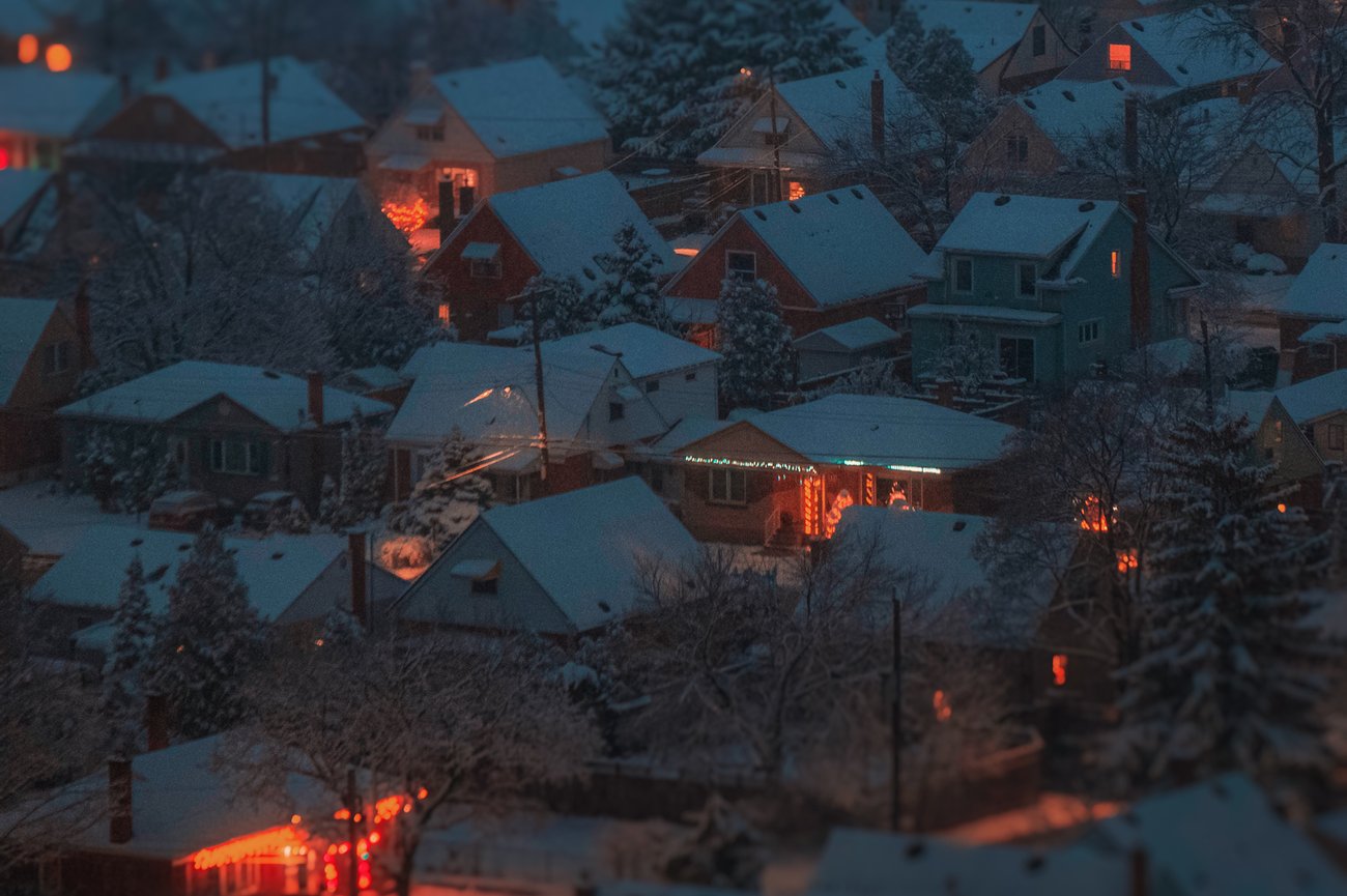 Snowy trees and roofs of neighborhood houses at night with several lit up in Christmas lights