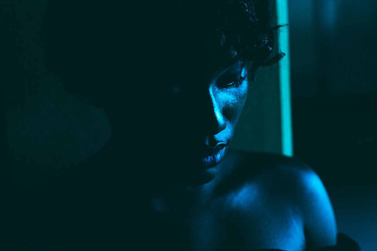 Black woman in shoulderless dress looking down in blue lit room