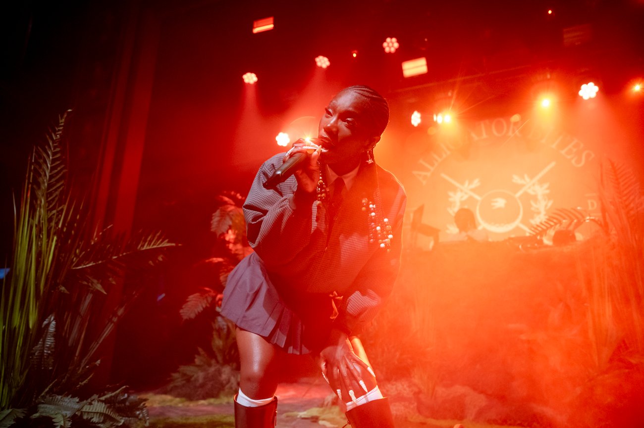 Rapper Doechii performing on stage lit in red light and decorated with plants