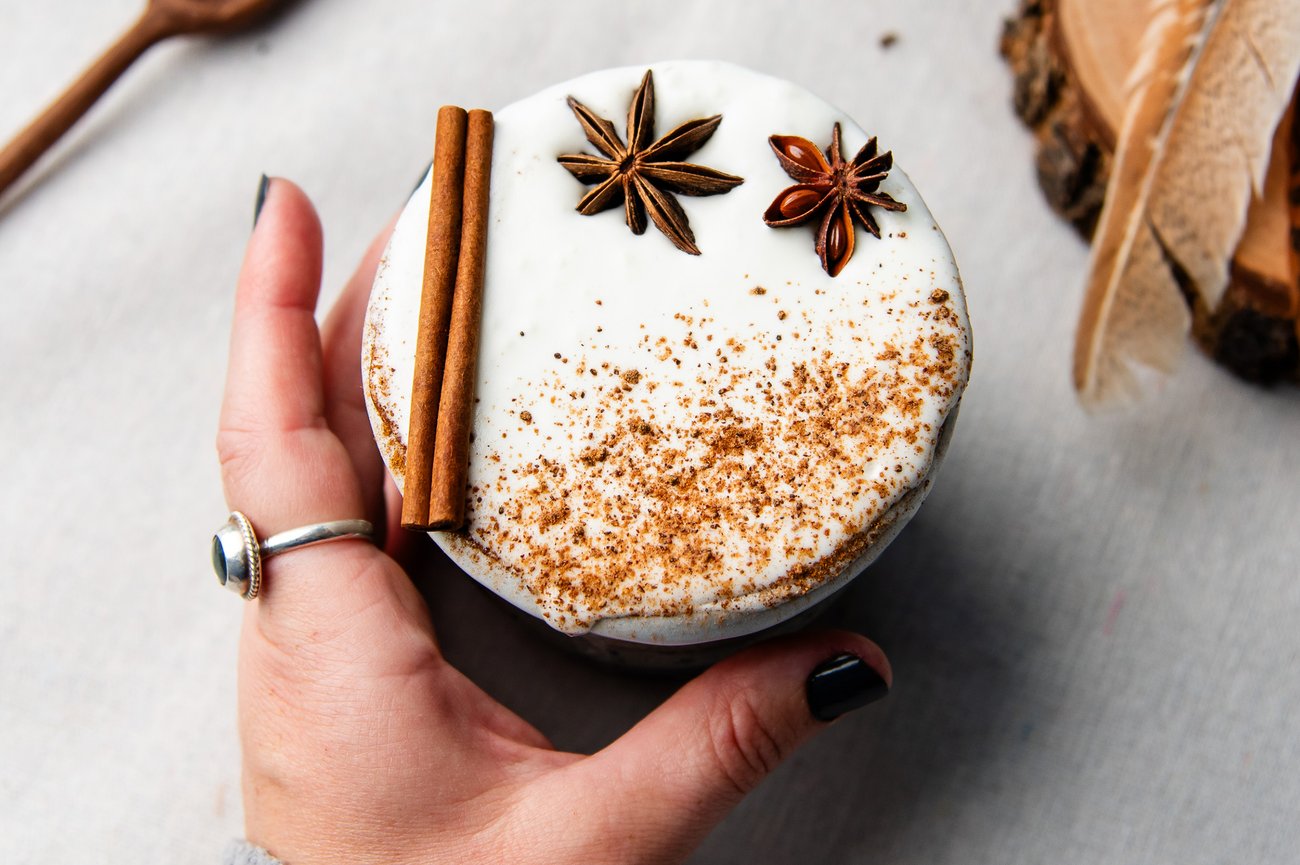 Top view of female hand reaching for frothy milk beverage topped with cinnamon stick and star anise
