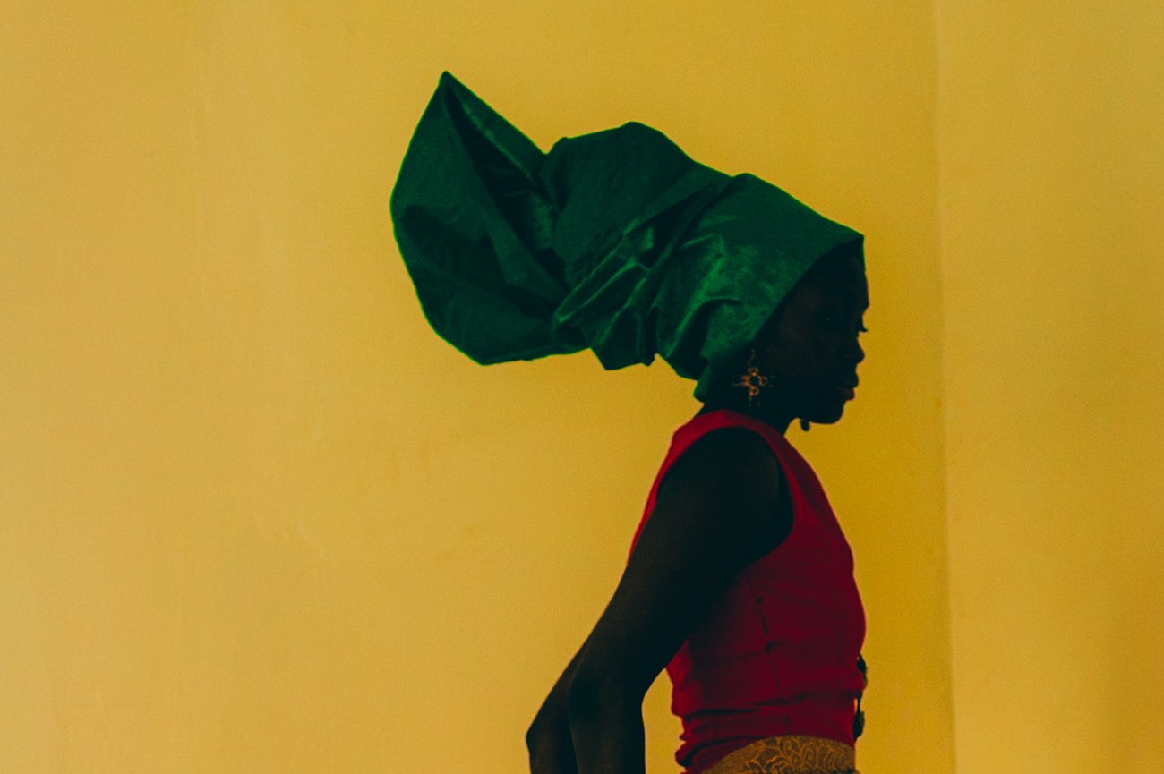 Black woman in red dress and green headdress in yellow room